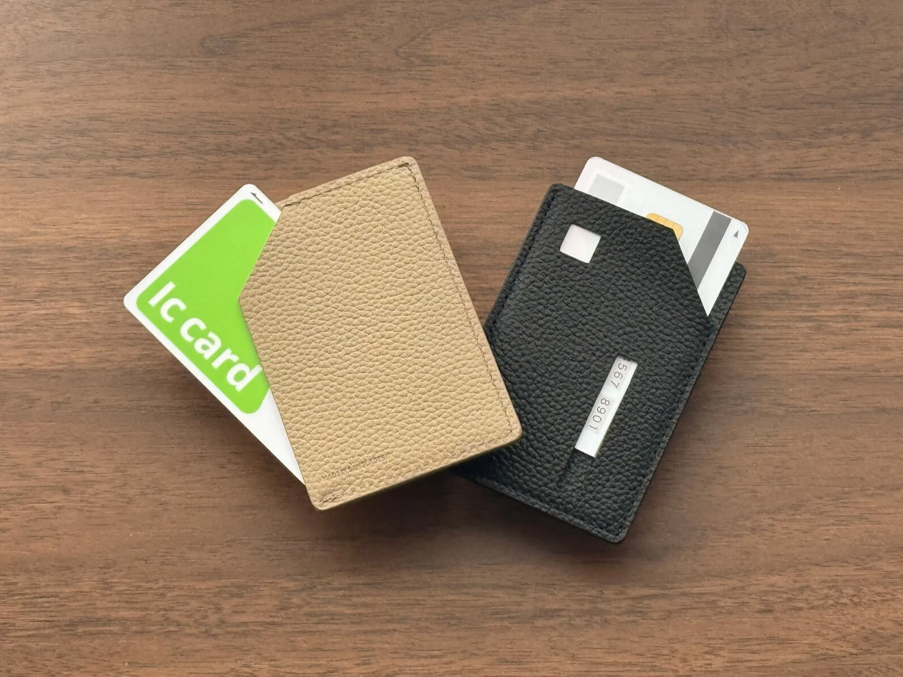 木製のテーブルの上に置かれた、ベージュと黒のカードケースの画像